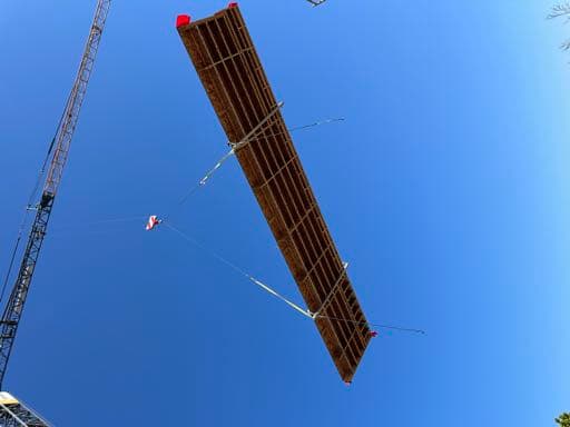 Wall panel suspended from crane against blue sky